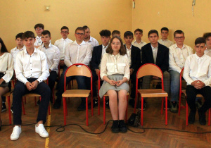 Uczniowie klasy ósmej siedzący na krzesłach, pozują do zdjęcia grupowego.