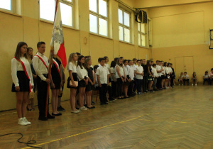 Odświętnie ubrani uczniowie stoją w rzędzie podczas uroczystości zakończenia roku szkolnego.