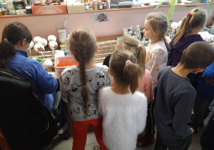 Dzieci przyglądają się pracy pani dekorującej ozdoby choinkowe.
