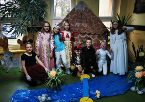 Dzieci w strojach postaci z bajek pozują do zdjęcia na tle dekoracji bajkowej.