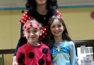Nauczycielka przebrana w strój Myszki Minnie pozuje do zdjęcia z dziewczynką w stroju biedronki i syrenki.