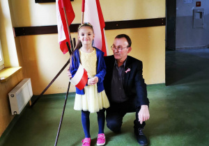 Dziewczynka z Ukrainy, ubrana w barwy narodowe swojego kraju, pozuje do zdjęcia z nauczycielem historii. W dłoni trzyma chorągiewkę biało- czerwoną.