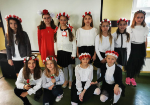 Dziewczynki ubrane w barwy narodowe Polski i wianki na głowach pozują do zdjęcia.