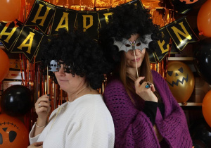 Nauczycielki w czarnych perukach i okularach Halloweenowych na tle napisu Happy Halloween.