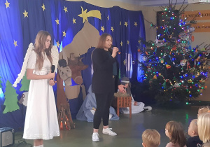 Uczennica klasy ósmej przebrana za anioła śpiewa kolędę wraz ze swoją siostrą.
