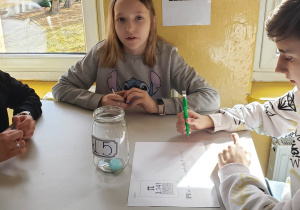 Grupa uczniów siedzi przy stoliku rozwiązując wspólnie zadanie matematyczne.