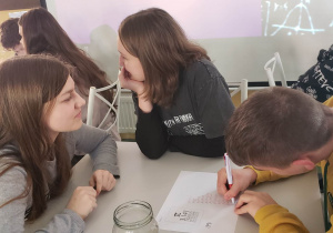 Grupa uczniów siedzi przy stoliku rozwiązując wspólnie zadanie matematyczne.
