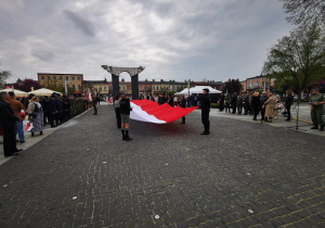 Harcerze z wielką biało-czerwoną flagą na tle pomnika na placu 11 Listopada w Łasku