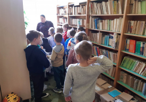 Uczniowie między półkami w bibliotece szkolnej.