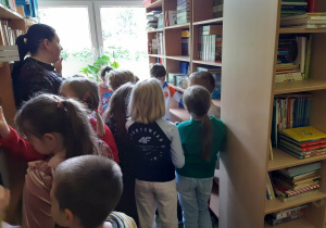 Uczniowie między półkami w bibliotece szkolnej.