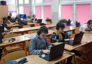 Uczniowie przy komputerach rozwiązują zadania konkursowe.