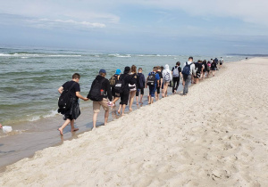 Uczestnicy wycieczki maszerują brzegiem morza.