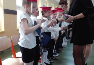 Wychowawca klasy oraz przewodnicząca Samorządu Uczniowskiego wręczają uczniom dyplomy i szkolne legitymacje.