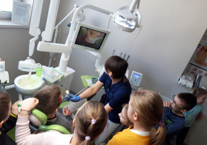 Uczeń siedzi na fotelu dentystycznym. Higienistka za pomocą kamery pokazuje uśmiech ucznia na ekranie.