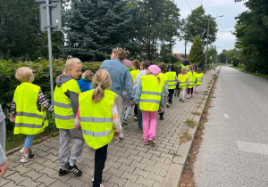 Dzieci ubrane w kamizelki odblaskowe udają się na spacer.