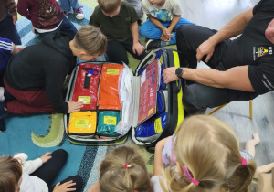 Dzieci z ciekawością przyglądają się dużej torbie z akcesoriami do udzielania pierwszej pomocy.