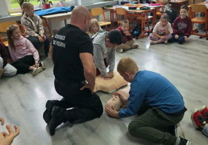 W asyście strażaka dzieci ćwiczą udzielanie pierwszej pomocy na fantomie.