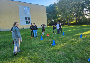 Chłopcy na boisku szkolnym rywalizują w konkurencjach sprawnościowych przygotowanych przez dziewczyny.