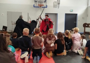 Dzieci oglądają walkę dwóch rycerzy na scenie.