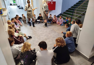 Dzieci siedzą w dużym kole. W środku dwie harcerki czuwają nad właściwym przebiegiem zabawy.