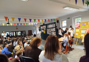 Uczniowie odgrywają scenkę i recytują okolicznościowe teksty, składając życzenia nauczycielom podczas szkolnych obchodów Dnia Edukacji Narodowej.
