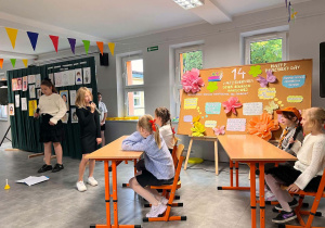 Uczniowie odgrywają scenkę i recytują okolicznościowe teksty, składając życzenia nauczycielom podczas szkolnych obchodów Dnia Edukacji Narodowej.