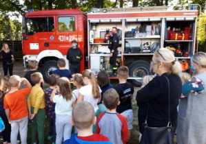 Dzieci słuchają strażaków i oglądają wyposażenie wozu strażackiego.