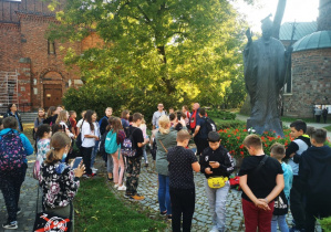 Uczestnicy wycieczki stoją przed pomnikiem Jana Pawała II.