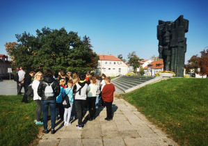 Uczestnicy wycieczki gromadza się przed pomnikiem.