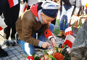 Uczeń klasy 5 zapala znicz przy pomniku walczących o niepodległość Polski.