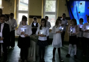 Uczniowie klasy drugiej przezentują taniec, trzymając w rękach zapalone lamki; na scenie panuje półmrok.