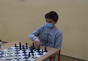 Uczeń siedzi przy planszy szachowej, wykonuje ruch.