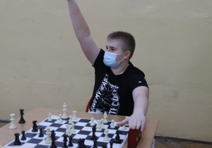 Uczeń siedzący przy stole szachowym podnosi rękę do oganizatorów konkursu.