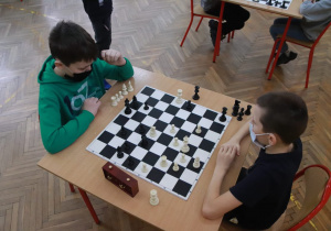 Dwóch uczestników konkursu rozgrywa partię szachową. Jedna z nich przestawia pionki na szachownicy.