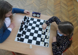 Dwie uczestniczki konkursu rozgrywają partię szachową. Jedna z nich przestawia pionki na szachownicy.