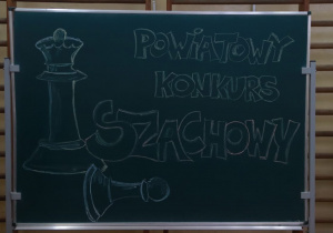 Na tablicy kredowej narysowano duże pionki szachowe. Obok rysunku widnieje napis: Powiatowy Konkurs Szachowy.