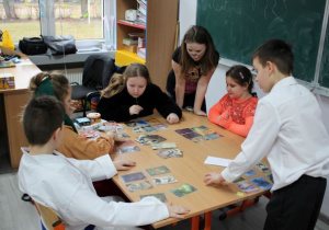 Grupa uczniów gromadzi się przy stole, na którym widać karty do gry.